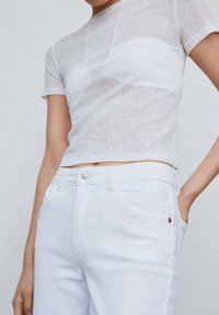 Top corto ajustado blanco de manga corta hecho de una tela suave y texturizada. Combinado con jeans blancos de pierna recta y cintura alta que cuentan con un botón de metal y un detalle de logo rojo.