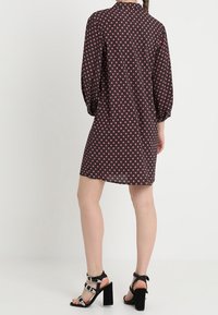 Black dress with pink geometric pattern, long sleeves, and button collar. Worn with strappy black heeled sandals featuring decorative studs.