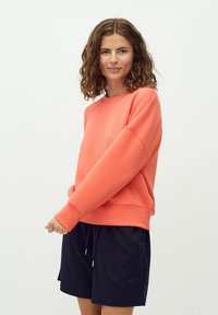Felpa in corallo con collo rotondo e maniche lunghe, abbinata a pantaloni corta blu navy. Tessuto morbido e vestibilità rilassata, con polsini e orlo a costine.