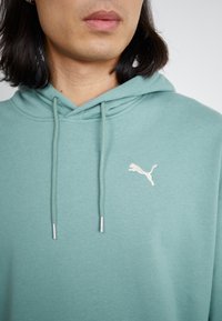Felpa verde chiaro realizzata in tessuto morbido, con tasca a marsupio, cordini e un piccolo logo Puma bianco sul lato sinistro del petto.