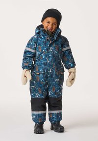 Sininen kuviollinen toppapuku, jossa eläinaiheisia kuvioita, huppu, heijastinnauhat ja mustat yksityiskohdat. Valkoiset lapaset ja mustat saappaat täydentävät asun.