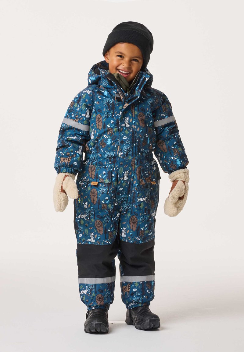 Sininen kuviollinen toppapuku, jossa eläinaiheisia kuvioita, huppu, heijastinnauhat ja mustat yksityiskohdat. Valkoiset lapaset ja mustat saappaat täydentävät asun.