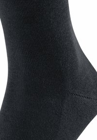 Schwarze Socke aus einem glatten, dehnbaren Material. Sie verfügt über eine gerippte Textur und eine nahtlose Zehenpartie mit verstärktem Fersenbereich für Langlebigkeit.