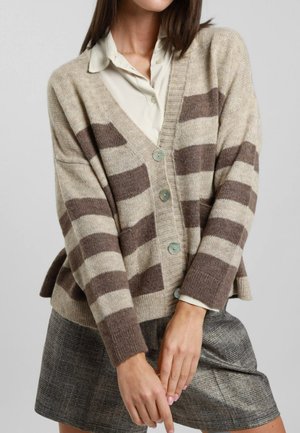 Cardigan lavorato a maglia beige con strisce marroni, scollatura a V, bottoni anteriori e spacchi laterali. Indossato sopra una blusa chiara e una gonna texturizzata.