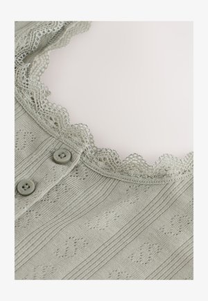 Vêtement en tricot gris présentant un col en dentelle à bords festonnés, deux boutons de fermeture et un motif texturé avec des rayures horizontales.