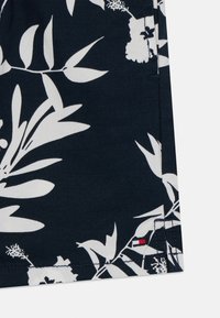 Marineblå shorts med et hvitt blomsterdesign, laget av lett stoff. Merkbar rød aksent ved kanten, med sydd detaljer.