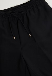 Pantalons de jogging noirs avec une taille élastique et un cordon de serrage. Caractéristiques d'un tissu lisse et texturé avec des embouts métalliques sur le cordon.