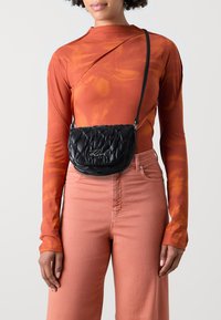Black quilted leather crossbody bag with a rounded shape. Features silver hardware and a decorative logo on the front.