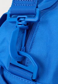 Μπλε υφασμάτινο σακίδιο πλάτης σε κοντινό πλάνο με ανθεκτική πλαστική αγκράφα και φερμουάρ, διαθέτοντας υφή στην επιφάνεια και ενισχυμένες ραφές.