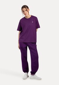 Set di maglietta e pantaloni tuta abbinato in viola, con maniche corte, vestibilità rilassata, polsini elastici e un discreto dettaglio del logo sul petto.