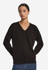 Schwarzer V-Ausschnitt-Pullover aus weichem Strickstoff mit geripptem Kragen und Bündchen. Bequeme Passform mit langen Ärmeln und gerader Säume.