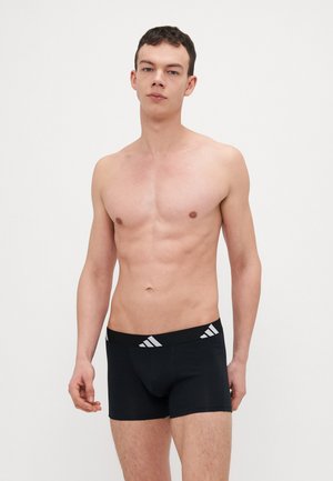 Schwarze Boxer-Briefs mit einem breiten elastischen Bund, der drei weiße Streifen aufweist. Der Stoff wirkt glatt und hat eine enganliegende Passform.