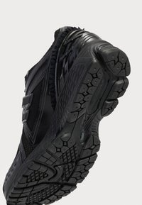 Black athletic shoe with a textured, patterned outsole. Features mesh panels and synthetic accents. Notable for the tread design and lightweight construction.