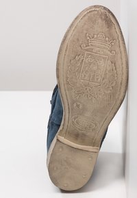 Niebieska skórzana podeszwa buta z teksturowanym spodem, z okrągłym logo i misternym tłoczonym wzorem. Rozmiar 36 zaznaczony.