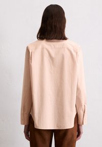 Camicia a maniche lunghe rosa chiaro con silhouette boxy, yoke posteriore e polsini con bottoni, realizzata in un morbido tessuto misto cotone.