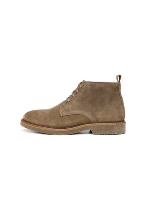 Brown suede ankle boots feature a rounded toe, two eyelets for laces, and a textured rubber sole. A looped tab is at the back for easy wear.
