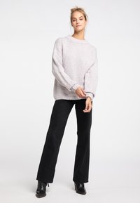 Pulover tricotat texturat de culoare gri deschis, cu o croială lejeră, manșete cu striuri și un decolteu larg, asortat cu pantaloni negri evazați și cizme negre până la glezne.