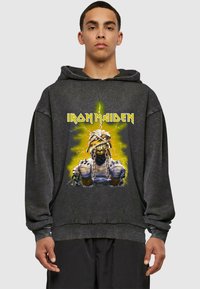 Svart oversized hettegenser med grafisk design av en bandkarakter med kjeder og gule lynaksenter. Mykt stoff med en avslappet passform.