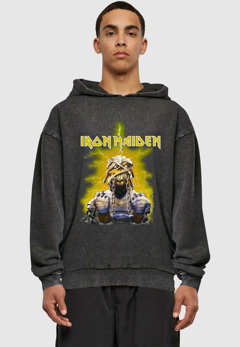 Svart oversized hettegenser med grafisk design av en bandkarakter med kjeder og gule lynaksenter. Mykt stoff med en avslappet passform.