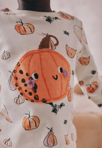 Hvid sweatshirt pyntet med farverige græskar- og dyreprints. Har et orange, broderet græskar-patch på forsiden med bløde detaljer.