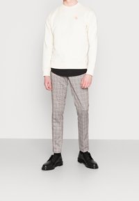 Sudadera de cuello redondo crema con un pequeño logotipo, combinada con pantalones de cuadros gris y negro de corte slim y botas negras con cordones.