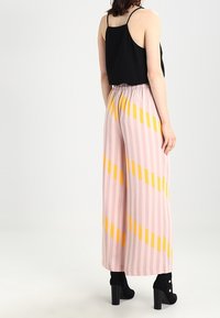 Černý bezramínkový top v kombinaci s vysokými kalhotami širokého střihu s růžovými pruhy a diagonálními žlutými akcenty. Texturovaná látka a elastický pas.