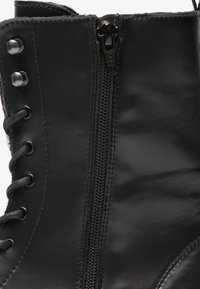 Bota de couro preto com fecho lateral, ilhós de metal e atacadores. A superfície tem uma textura suave e um acabamento brilhante.