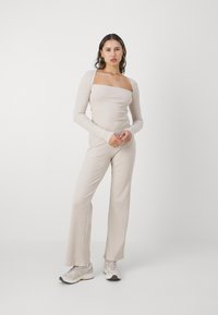Beige ribstrikket top med lange ærmer og firkantet halslinje, parret med matchende ribstrikkede flarebukser. Båret med lyse sneakers.