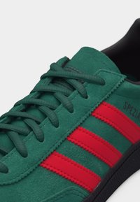 Πράσινο σουέτ αθλητικό παπούτσι με κόκκινες ρίγες και ταιριαστά πράσινα κορδόνια, με μαύρη σόλα και τη λέξη "SPEZIAL" στο πλάι.