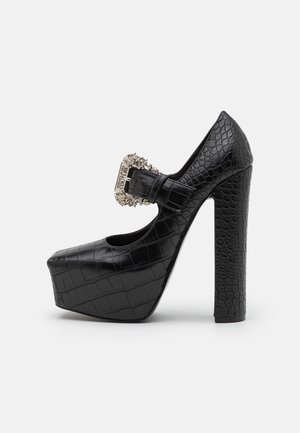 Chaussure à plateforme noire à talons hauts avec une texture croco, dotée d'une boucle décorative en argent et d'un épais talon carré.