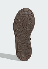 Sola de um ténis, borracha castanha com padrões texturizados, realces circulares e um logótipo. Apresenta várias seções de aderência para tração.