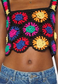 Haut court en crochet noir orné de motifs floraux circulaires colorés en rouge, bleu, vert, jaune et rose, avec des bords festonnés.