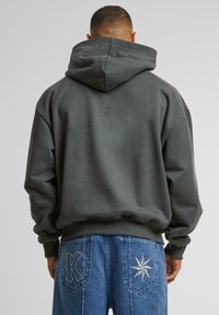 Sudadera gris oscuro con una capucha grande, corte ligeramente holgado y dobladillo acanalado. Combinada con jeans azules que presentan un bordado de estrellas blancas y una "K" en los bolsillos.