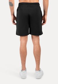 Pantalones cortos deportivos negros con una cinturilla elástica, bolsillos laterales y una textura suave, combinados con zapatillas blancas.