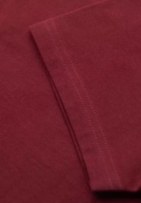 Burgundská tkanina ukazující přehnutý okraj s viditelným stehem, hladký povrch a čisté linie, zdůrazňující její jednoduchý design.