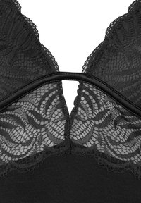 Bralette in pizzo nero con delicati motivi floreali, base in tessuto liscio, spalline regolabili e design a oblò sul retro.