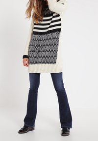 Sweter dzianinowy z czarno-białym paskowanym wzorem, z teksturowaną dolną częścią. W połączeniu z ciemnoniebieskimi dzwonami i czarnymi butami.