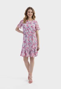 Blumenkleid mit rosa und blauen Farbtönen, kurzen Rüschensäumen, tailliertem Gürtel und einem flared Rüschensaum. Getragen mit rosa Riemchenschuhen.
