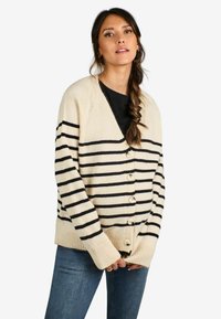 Cardigan a righe beige con strisce orizzontali nere, scollo a V, maniche lunghe e sette bottoni sulla parte anteriore. Polsini e orlo a coste.