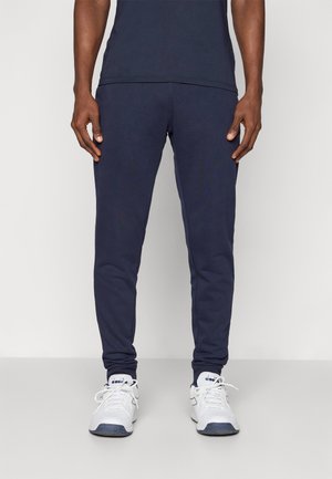 Marineblauwe sportieve joggers met een slim fit, gemaakt van zacht materiaal, voorzien van elastische boorden en zakken, gedragen met witte sneakers.