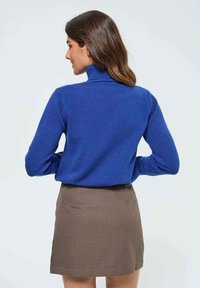 Pull à col roulé bleu en tricot doux, associé à une mini-jupe écossaise marron. Tissu texturé avec des manches et un col cintrés.