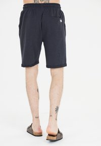 Tummansiniset puuvillashortsit, joissa on joustava vyötärö, käärityt lahkeet ja sivutaskut, ja joissa on pieni logopatchi takana.