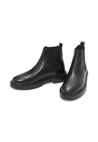 Botas Chelsea de cuero negro con paneles elásticos en los lados y tiradores, con punta redondeada y suela plana de goma, textura suave.