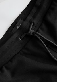 Sorte shorts med elastik i taljen og snøre lukning. Blødt stof med en ensfarvet tekstur. "NEXT" label syet på livet.