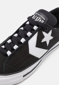 Sapatilhas de lona pretas com o logótipo de estrela branca e detalhes. Apresentam um upper texturizado, atacadores pretos e uma sola de borracha.