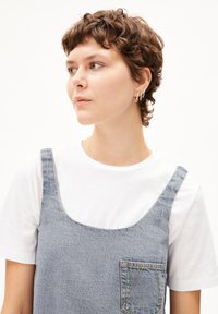 Lichtblauwe denim jurk met een ronde hals, dunne bandjes en een borstzak; gedragen over een eenvoudige witte T-shirt.