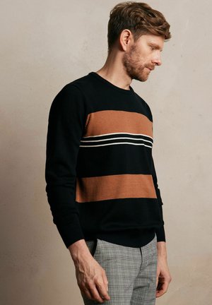 Czarny sweter w poziome brązowe i białe paski, okrągły dekolt, ściągacze przy rękawach, zestawiony z szarymi spodniami w kratę, gładka faktura.