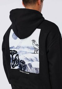 Hoodie nera con una stampa grafica sul retro che presenta un paesaggio in bianco e nero, un'illustrazione di un uccello e la scritta "PROJECT X PARIS" in fondo.