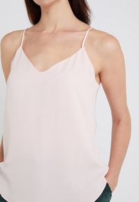 Débardeur rose clair sans manches avec un décolleté en V, fabriqué à partir d'un tissu doux, présentant des bretelles fines et une coupe ample. Design minimaliste sans motifs.