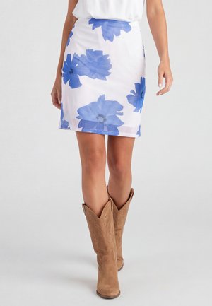 Witte rok met grote blauwe bloemenprint, gedragen met tan suède cowboylaarzen en een ingestopte witte top, zichtbaar van taille tot voeten.